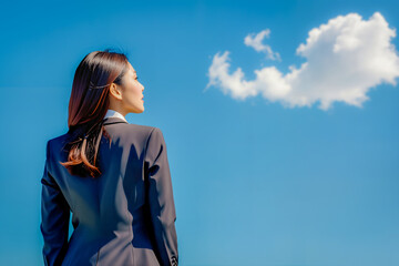 Plakat Back view of businesswoman in a suit looking up at a clear blue sky.