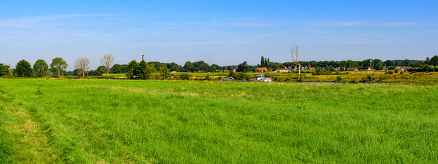 Panorama photo mid summer of a landscape at the edge of the river "De Maas" Noord Brabant, Netherlands. Surrounded by green nature and a clear blue sky.