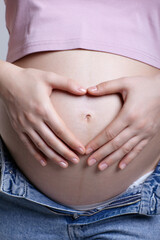 Female on 6th month of pregnancy. Woman touching with hands her naked belly and shows heart sign.