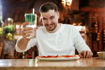 With mojito. Man is sitting in the restaurant and eating a pizza