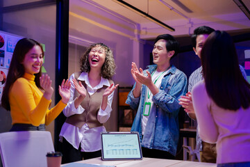 Asian young creative professional successful businesswoman staff standing greeting finishing presentation while male and female colleagues clapping hands together admire compliment in office at night.