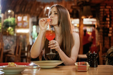 Red cocktail, drinking. Woman is in the restaurant with food and drink