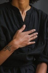 Close-up of a person wearing black clothing, with a hand on their chest signifying a moment of self-connection and reflection