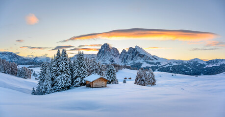 Panoramic view on Alpe di Siusi meadow with small wooden log cabin and first snow. Snowy hills with...