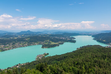 Obraz premium Aerial panoramic view of Lake Wörthersee seen from Pyramindenkogel in Carinthia, Austria. Serene turquoise waters, lush green forests and rolling hills of Austrian Alps. Charming lakeside village