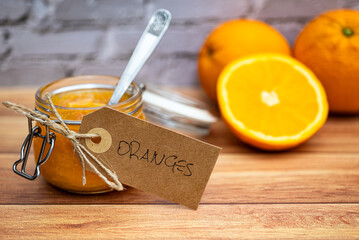 Glass jar with delicious homemade orange marmalade on a wooden table. Jar with vintage brown cardboard label attached with string. Sweet break with homemade orange marmalade.