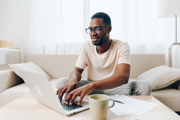 Smiling African American Freelancer Working on Laptop in Modern Home Office on Sofa He is Typing...