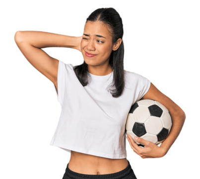 Young Filipino woman with soccer ball touching back of head, thinking and making a choice.