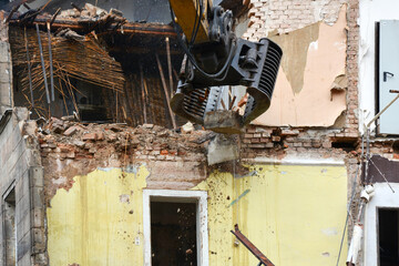 An excavator using a manipulator dismantles and destroys an old house. Construction site