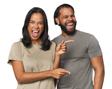 Young Latino couple in studio pointing with forefingers to a copy space, expressing excitement and desire.
