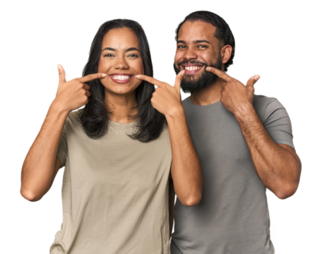 Young Latino couple in studio smiles, pointing fingers at mouth. - Powered by Adobe