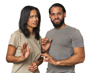 Young Latino couple in studio rejecting someone showing a gesture of disgust.