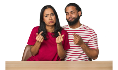 Seated young Latino couple at table showing that she has no money.