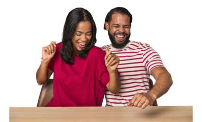 Seated young Latino couple at table dancing and having fun.
