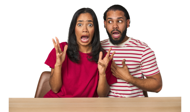 Seated young Latino couple at table screaming to the sky, looking up, frustrated.