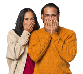 Young Latino couple in studio laughing about something, covering mouth with hands.