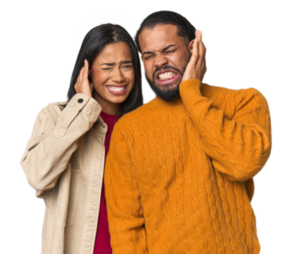 Young Latino couple in studio covering ears with hands.