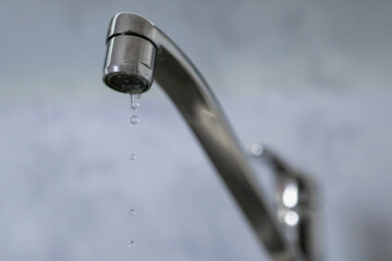 A drop of water drips from a leaky faucet. Close-up of a water dripping from a faucet