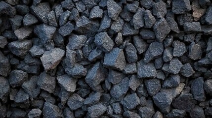 A collection of dark gravel rocks scatters across a surface, showcasing their rough textures and varying sizes, typically used in construction