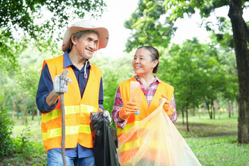 older adult husband and wife in safety vest walking in the garden collecting and sorting waste,asian senior couple spend holiday time doing volunteer activity collecting and sorting waste in the park