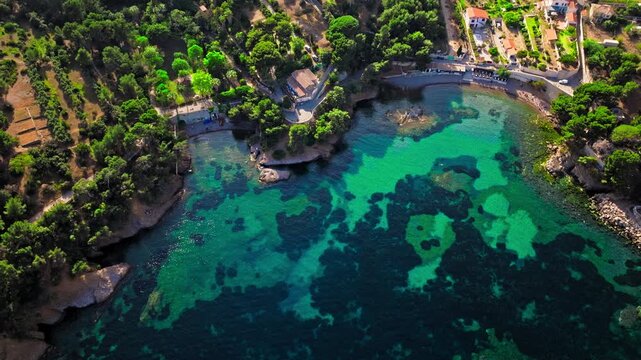 Aerial view of a Botanical garden with Snug Cove framed by rugged cliffs in Parc du Mugel. View from above of swimming off a pebble beach with turquoise clear water in France.