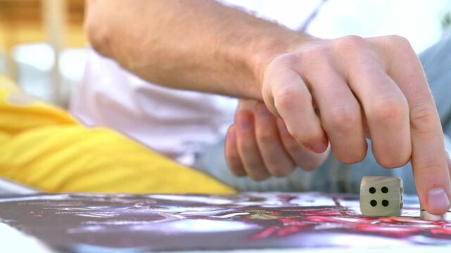 Throwing game dice and moving chip in board game, male hands close-up, front view.