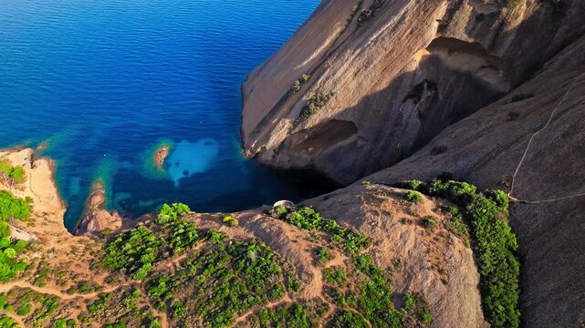 Aerial view of a Botanical garden with Snug Cove framed by rugged cliffs in Parc du Mugel. View from above of swimming off a pebble beach with turquoise clear water in France.