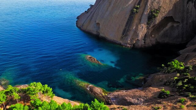 Aerial view of a Botanical garden with Snug Cove framed by rugged cliffs in Parc du Mugel. View from above of swimming off a pebble beach with turquoise clear water in France.
