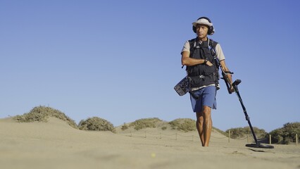 Young adult treasure hunter advancing towards target while searching for jewellery, with the Maspalomas sand dunes in the background.