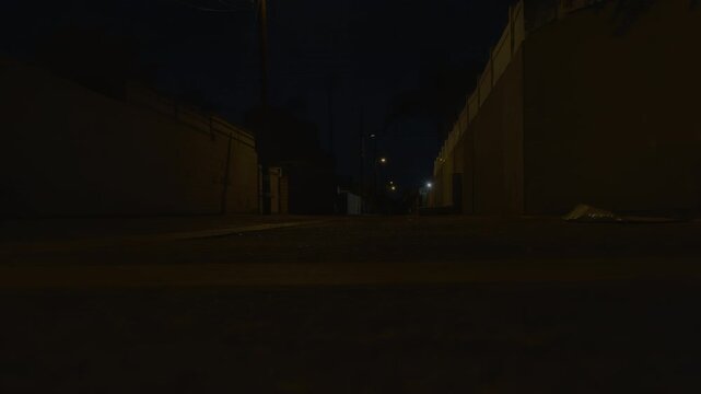 Low angle shot of dark narrow street with scarce lanterns and few buildings. Dimly lit night alley at the edge of the town.