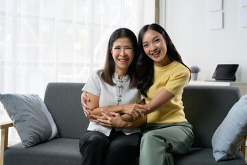 Happy Mother and Daughter Sitting on Sofa at Home, Smiling and Embracing Each Other