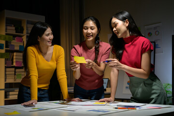 Fototapeta premium Young Women Collaborating on Creative Project in Modern Office Setting at Night