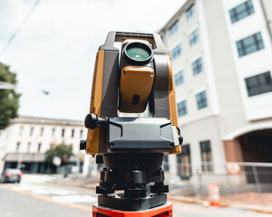 land surveying total station instrument on a tripod with a building in the background