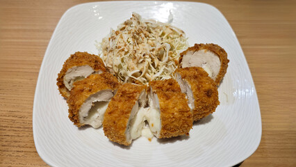 Crispy Tonkatsu Served with Shredded Cabbage on White Plate with Wooden Table Background in Restaurant Setting