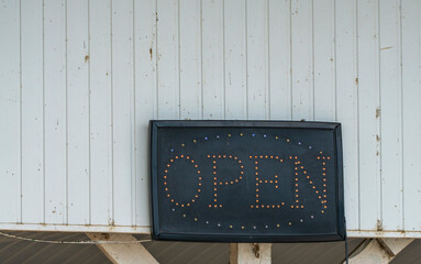 "Open" , Sign Electric Device Black Board Information in Front of Store with White Wooden Planks Background.