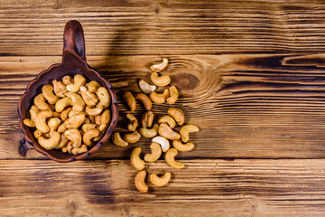 Ceramic bowl with roasted cashew nuts on a wooden table. Top view