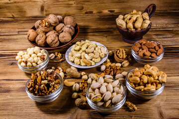 Various nuts (almond, cashew, hazelnut, pistachio, walnut) in bowls on a wooden table. Vegetarian meal. Healthy eating concept