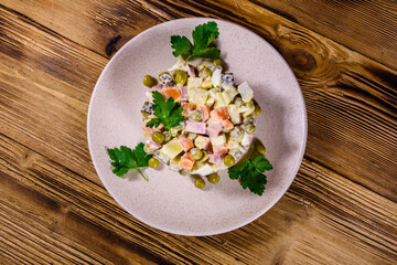 Ceramic plate with russian traditional new year salad olivier on a wooden table. Top view