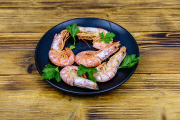 Plate with prepared shrimps and parsley leaves on a wooden table