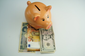 top view of a piggy bank on several dollar, euro and yen bills as a currency saving concept