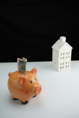 Vertical detail photo of a piggy bank with several yen bills inserted inside and next to a residential building as a concept of saving for the purchase of housing
