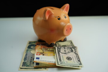 Horizontal photo of a piggy bank on several dollar, euro and yen bills as a currency saving concept