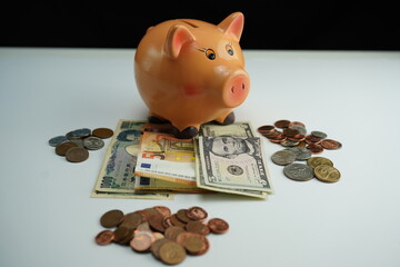 Horizontal photo of a piggy bank on several dollar, euro and yen bills and surrounded by coins of different currencies as a concept of buying and saving foreign currency