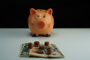 Several dollar, euro and yen bills surrounded by coins of different currencies with a piggy bank out of focus in the background as a concept of saving and buying foreign currency