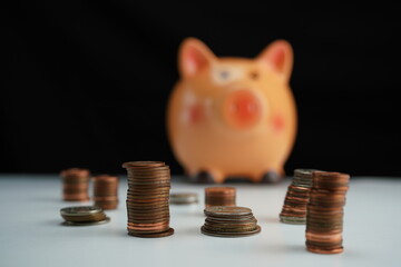 several piles of coins of different currencies in front of a piggy bank in the background in blur as a savings concept