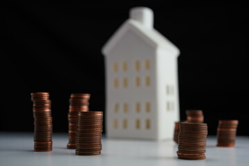 Horizontal photo of stacked coins of different currencies in front of a house as a concept of saving for home purchase