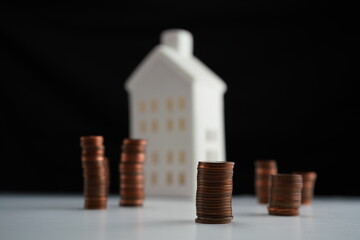 Stacked coins of different currencies in front of a house as a concept of saving for home purchase