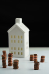 Vertical photo of stacked coins of different currencies in front of a house as a concept of saving for home purchase