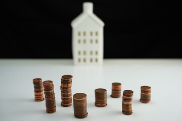 Overview with detail of stacked coins of different currencies in front of a house as a concept of saving for home purchase
