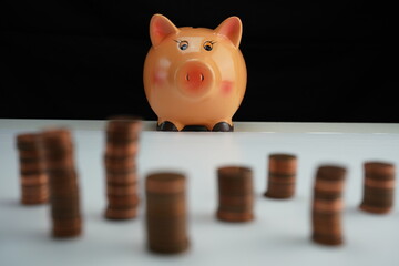 Stacked coins of different currencies out of focus in front of a piggy bank in focus in the background as a concept of saving for home purchase